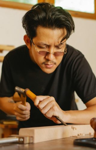 Focused artisan using tools to craft a wooden plank in a workshop setting.