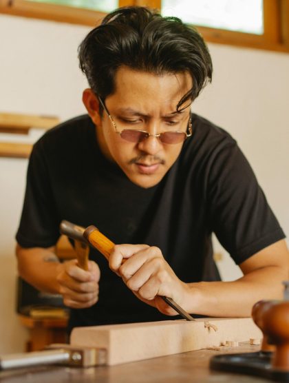 Focused artisan using tools to craft a wooden plank in a workshop setting.